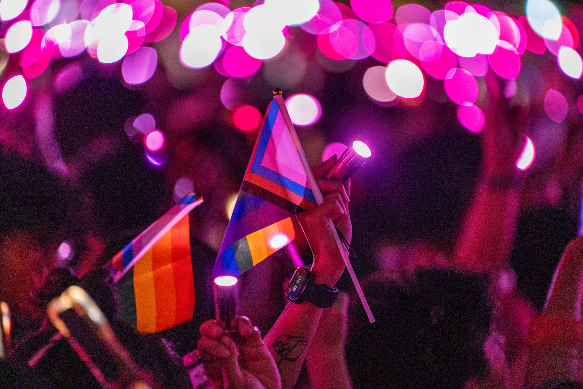 A progress pride flag is held up in a sea of pink lights during Pink Dot.